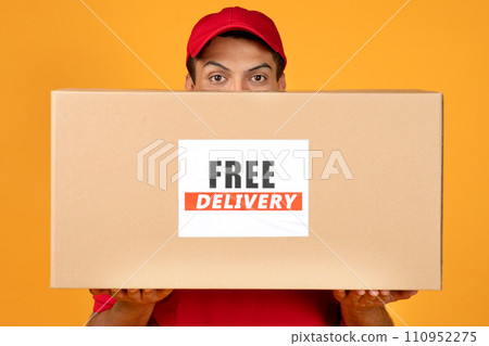 deliveryman peeking from cardboard box with Free Delivery label, studio 110952275