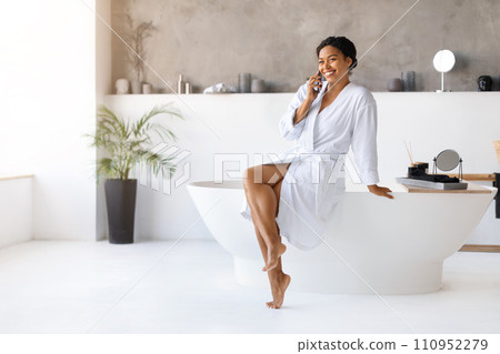 Beautiful Black Woman Wearing Bathrobe Talking On Mobile Phone In Modern Bathroom 110952279