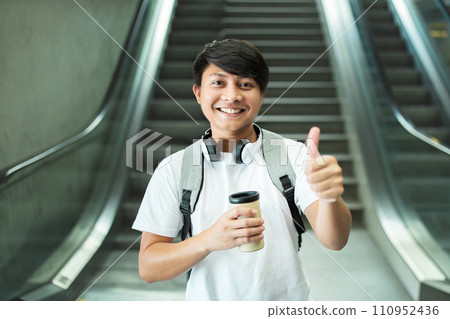 Cheerful young asian guy tourist drinking coffee, showing thumb up 110952436
