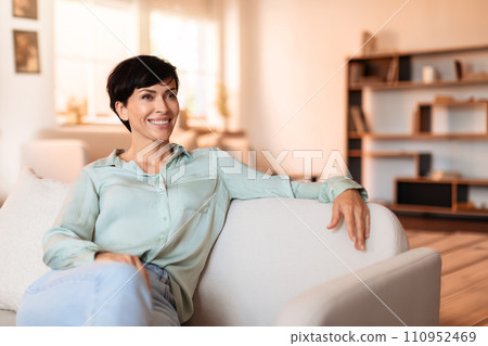 Brunette lady casually sitting in modern living room on sofa 110952469