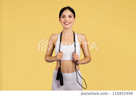 Caucasian slim woman in sportswear with skipping rope, enjoy workout, posing isolated on yellow studio background 110952499