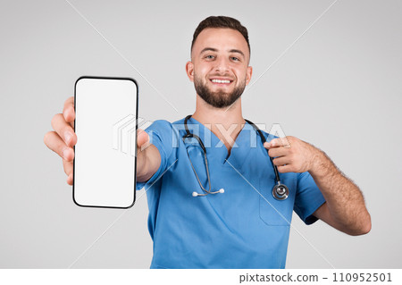 Cheerful doctor man showing blank phone screen and pointing at it 110952501