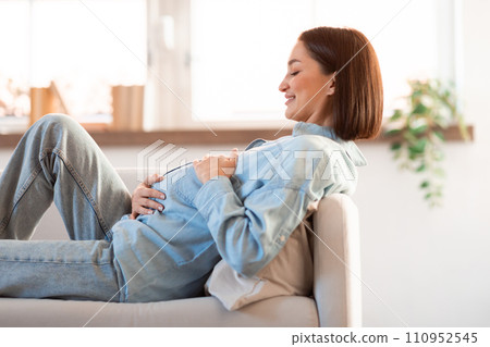 Pregnant Young Woman Hugging Belly Resting On Sofa At Home 110952545