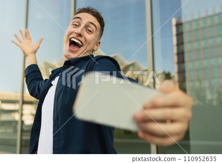 Glad excited millennial caucasian man blogger in casual make selfie on phone, walk in city 110952635