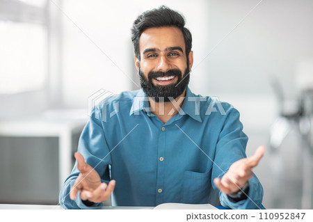 Cheerful indian bearded man in blue shirt smiling and gesturing at camera Cheerful indian bearded man in blue shirt smiling and gesturing at camera 110952847