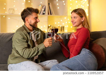 Happy couple toasting with wine glasses in a cozy room Happy couple toasting with wine glasses in a cozy room 110952857