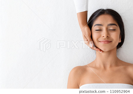 Joyful young indian woman relaxing during face lifting massage 110952904
