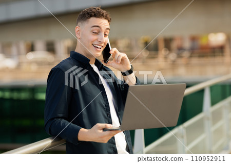 Positive confident young caucasian man in casual work with laptop, call by smartphone in office, outdoor Positive confident young caucasian man in casual work with laptop, call by smartphone in office, outdoor 110952911