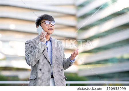 Young Asian specialist man talking via smartphone in hand outside 110952999