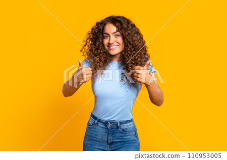 Happy curly woman giving two thumbs up on yellow Happy curly woman giving two thumbs up on yellow 110953005