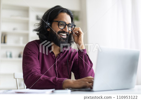 Handsome Young Indian Man Wearing Headset And Eyeglasses Watching Webinar On Laptop 110953122