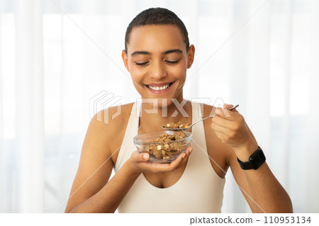 Smiling millennial latin lady in sportswear eat muesli cereal, enjoy breakfast Smiling millennial latin lady in sportswear eat muesli cereal, enjoy breakfast 110953134