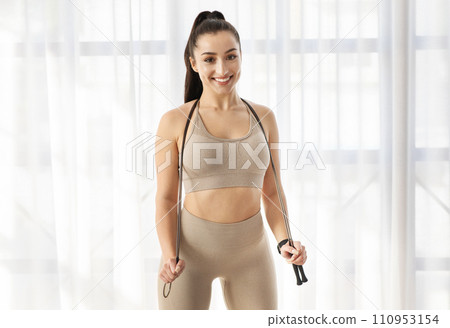 Beautiful well-fit brunette sportswoman posing with skipping rope indoors Beautiful well-fit brunette sportswoman posing with skipping rope indoors 110953154