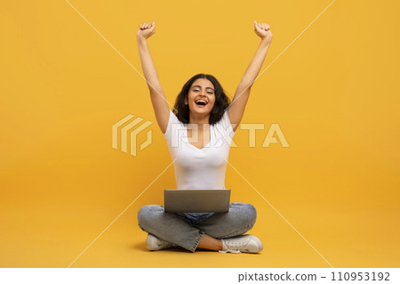Emotional young indian lady sitting on floor, using laptop Emotional young indian lady sitting on floor, using laptop 110953192