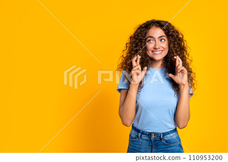 Woman with fingers crossed, hopeful look on yellow background 110953200
