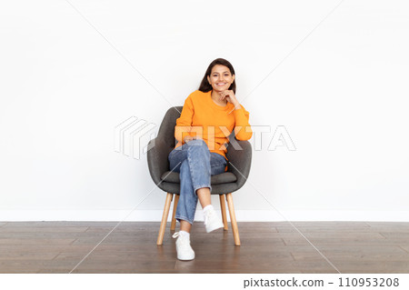 Cheerful young indian woman sitting in armchair over white background Cheerful young indian woman sitting in armchair over white background 110953208
