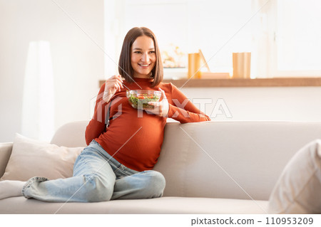 Pregnant lady enjoying fresh vegetarian salad with a smile indoor 110953209