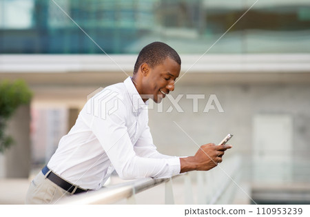 Smiling Black Businessman Leaning At Railing And Using Smartphone Outdoors Smiling Black Businessman Leaning At Railing And Using Smartphone Outdoors 110953239