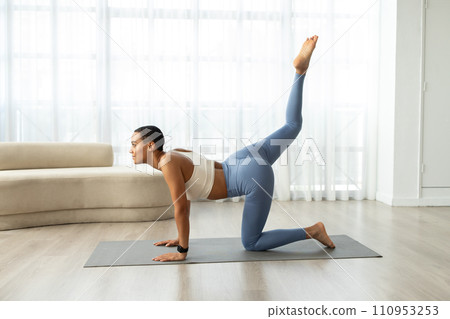 Focused slim young latin woman in sportswear doing legs exercises on mat, enjoy fitness in living room 110953253