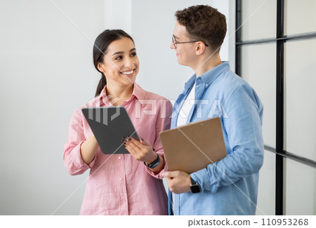 Happy young arab lady show tablet to european man manager boss with clipboard Happy young arab lady show tablet to european man manager boss with clipboard 110953268