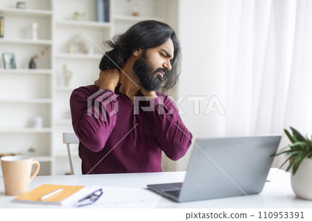 Tired Indian Freelancer Man With Neck Pain Sitting At Desk With Laptop 110953391