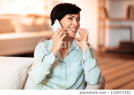 Middle aged lady chatting happily on her cellphone at home Middle aged lady chatting happily on her cellphone at home 110953392