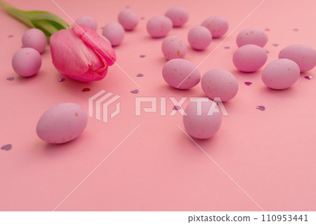 Easter card. Bright pink chocolate eggs scattered on pink background. Shimmering glowing hearts and delicate tulip. Easter and spring themes, use in marketing materials, packaging. Happy holidays Easter card. Bright pink chocolate eggs scattered on pink background. Shimmering glowing hearts and delicate tulip. Easter and spring themes, use in marketing materials, packaging. Happy holidays 110953441