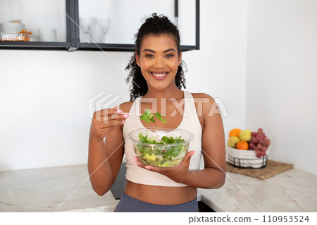 Young fitness woman enjoys fresh salad standing in modern kitchen 110953524