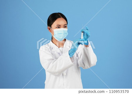 Vaccination. Asian doctor in medical mask looking at syringe in her hand Vaccination. Asian doctor in medical mask looking at syringe in her hand 110953570