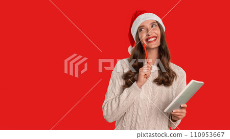 woman in Santa hat writes holiday wishlist in notebook, studio 110953667