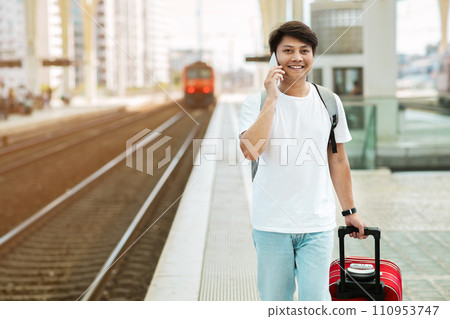 Happy guy tourist walking by train station, talking on phone Happy guy tourist walking by train station, talking on phone 110953747