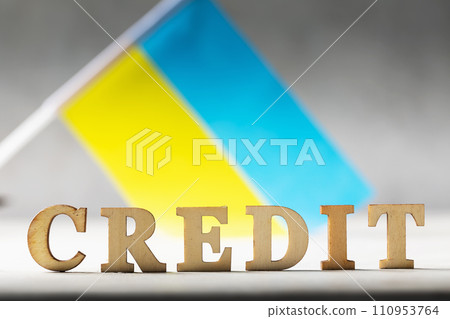 Text with wooden letters and Ukrainian flag on an abstract background, concept on the theme of the debt burden of the people of Ukraine 110953764