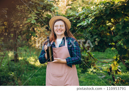 30s Woman in hat tasting red wine in vineyard. Portrait of pretty young woman holding bottle of wine on sunny day. Natural wine industry. Mockup for design 30s Woman in hat tasting red wine in vineyard. Portrait of pretty young woman holding bottle of wine on sunny day. Natural wine industry. Mockup for design 110953791