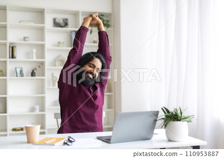 Relaxed Indian freelancer man taking break and stretching after working on laptop 110953887