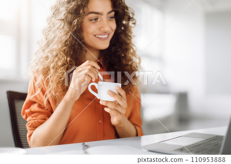 Curly-haired woman enjoying coffee at work 110953888