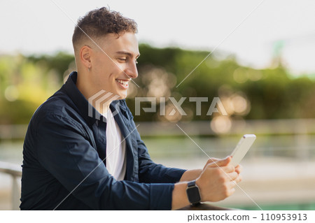 Glad millennial caucasian man in casual typing on mobile phone, walk in city, outdoor 110953913