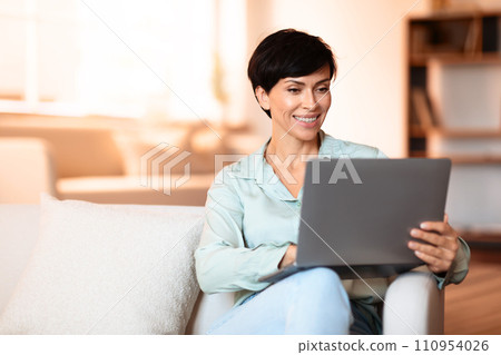 Woman comfortably working online from home via laptop indoor 110954026