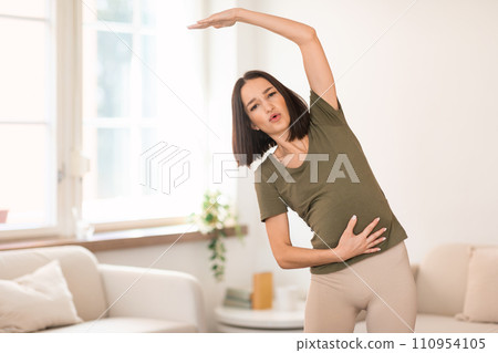 Pregnant lady exercising at home doing side bends raising arm 110954105