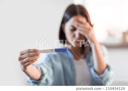 Upset lady holding positive pregnancy test at home, covering face Upset lady holding positive pregnancy test at home, covering face 110954120
