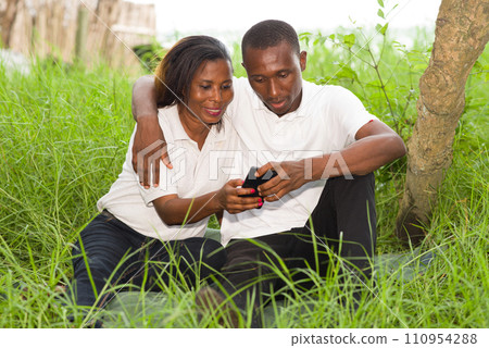 Happy couple using mobile phone in green grass 110954288