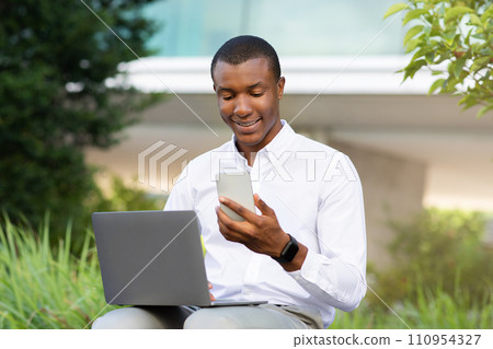 Modern Technologies For Business. Black Businessman Using Laptop And Smartphone Outdoors Modern Technologies For Business. Black Businessman Using Laptop And Smartphone Outdoors 110954327