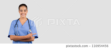 Glad european young doctor, nurse in blue uniform point finger at copy space Glad european young doctor, nurse in blue uniform point finger at copy space 110954456