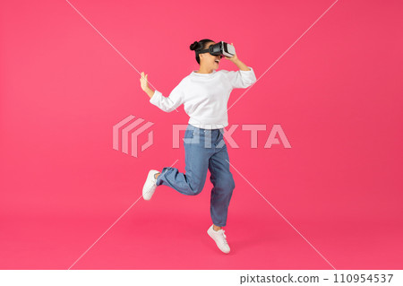 Cheerful asian woman wearing vr headset jumping joyfully in mid-air 110954537