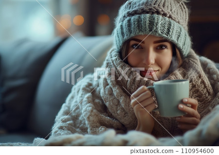 A woman in a cozy woolen hat, wrapped in a plush blanket, holding a steaming cup of tea, set in a comfortable and inviting living room A woman in a cozy woolen hat, wrapped in a plush blanket, holding a steaming cup of tea, set in a comfortable and inviting living room 110954600
