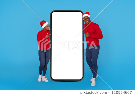 African couple in santa hats pointing at large phone, studio African couple in santa hats pointing at large phone, studio 110954667