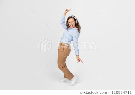 Cheerful european millennial woman in wireless headphones with open mouth, dance, listen music, sing song Cheerful european millennial woman in wireless headphones with open mouth, dance, listen music, sing song 110954711