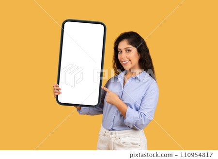 Smiling latin millennial brunette woman point finger at big smartphone with empty screen 110954817