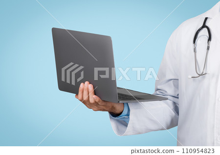 Doctor in white coat holding a laptop, blue background, closeup 110954823
