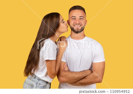 Cheerful millennial european woman in white t-shirt kiss strong man in cheek, enjoy romantic date 110954952