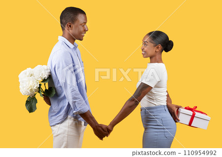 Black couple with flowers and gift celebrating lover's holiday, hiding surprises for each other behind their backs Black couple with flowers and gift celebrating lover's holiday, hiding surprises for each other behind their backs 110954992